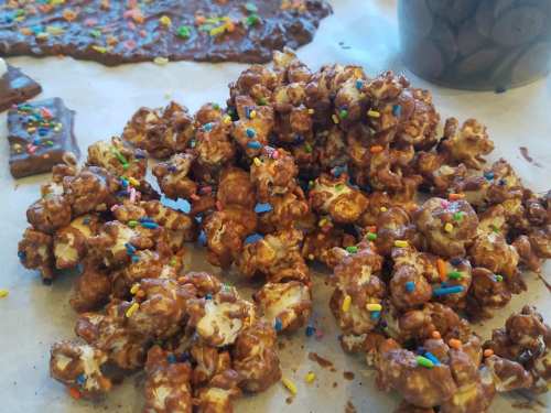 A close-up of chocolate-covered popcorn sprinkled with colorful candy bits on parchment paper.