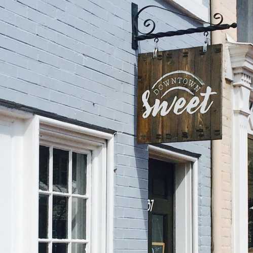 A wooden sign reading "Downtown Sweet" hangs outside a light blue building.