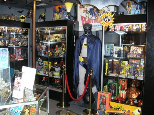 A display of Batman memorabilia, featuring a life-sized Batman figure and various toys in glass cases.