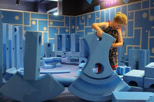 A child plays with large blue foam blocks in a colorful, interactive play area.