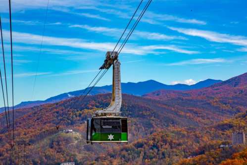 A scenic view of a cable car traveling over colorful autumn mountains under a blue sky.