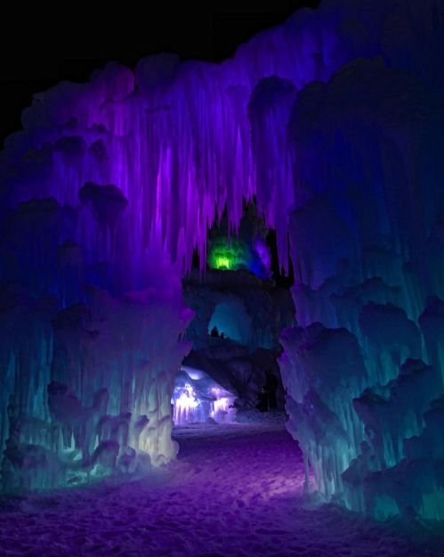 A colorful ice cave illuminated with purple and green lights, featuring icicles and a snowy floor.
