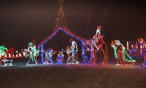 Colorful holiday lights depict a nativity scene with figures around a stable, set in a nighttime outdoor setting.