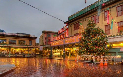 A festive farmers market with holiday decorations and a Christmas tree, reflecting on wet brick streets.