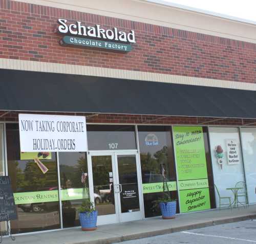 Exterior of Schakolad Chocolate Factory, featuring a sign for corporate holiday orders and a welcoming storefront.