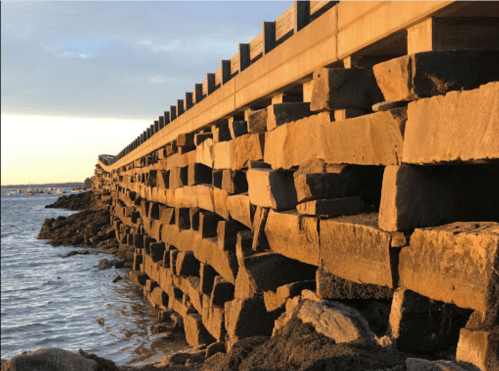 A stone pier extends into the water, illuminated by warm sunset light, with a calm sea and distant horizon.