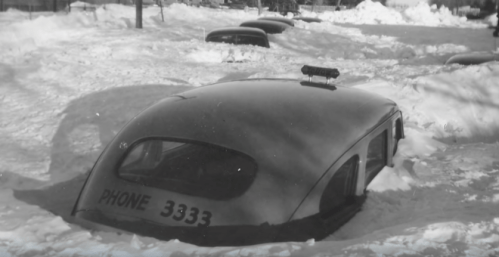 A vintage car partially submerged in deep snow, with only the roof and light visible.