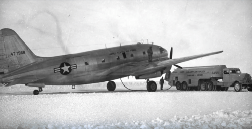 A vintage military aircraft refueling on a snowy landscape, with a fuel truck nearby.