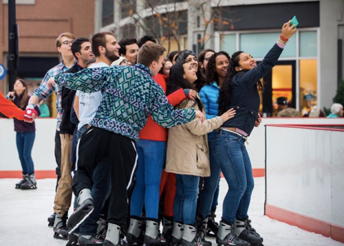 A group of friends poses for a selfie on an ice skating rink, smiling and enjoying their time together.