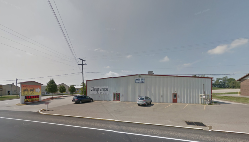 A metal building with "Clearance" signage, parked cars, and a nearby restaurant sign on a sunny day.