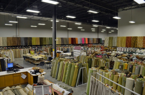 A spacious fabric store filled with rolls of various patterned and colored fabrics stacked on shelves and tables.