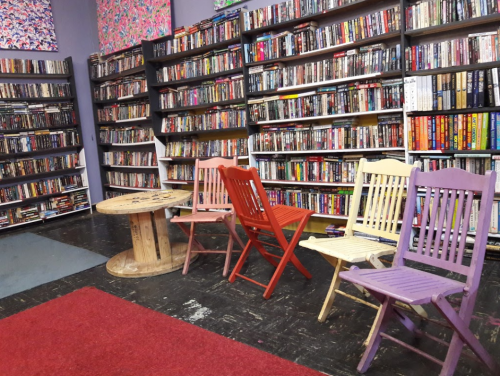 A cozy room with colorful chairs and shelves filled with DVDs and books, featuring a round wooden table.