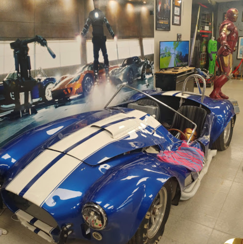 A blue sports car with white stripes, surrounded by superhero-themed decor and a wall mural of characters.