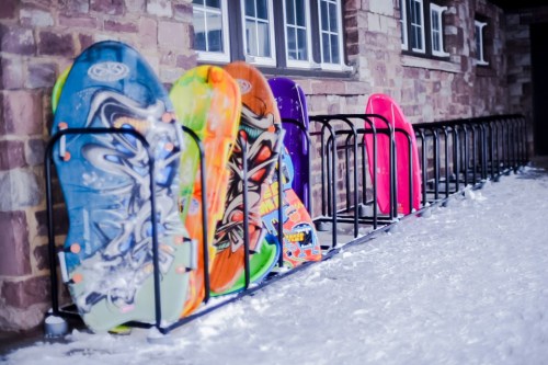 A row of colorful sleds lined up on a snowy surface next to a stone building.