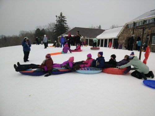 A group of people enjoying snow tubing on a snowy hill, with some sitting on colorful tubes and others in the background.