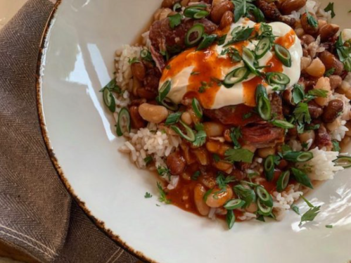 A bowl of rice topped with beans, meat, sour cream, and green onions, garnished with fresh herbs.