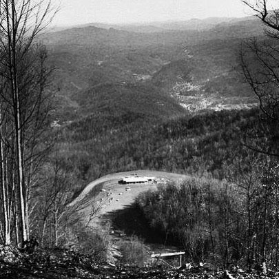 A black and white landscape showing rolling hills and a valley, with a small building visible in the distance.