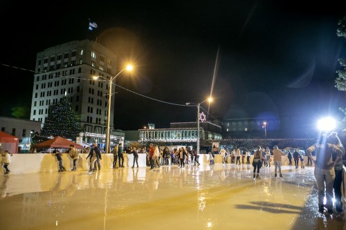 A bustling outdoor ice skating rink at night, with people skating and festive lights in the background.