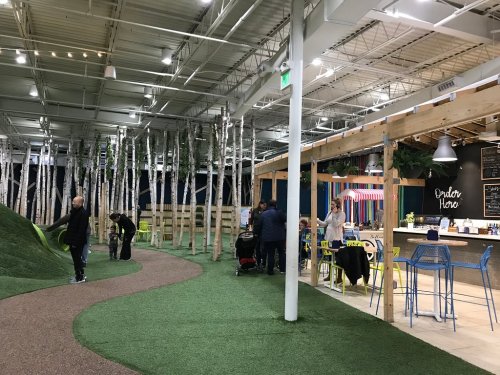 A spacious indoor area with artificial grass, trees, and a café, featuring people socializing and enjoying the environment.