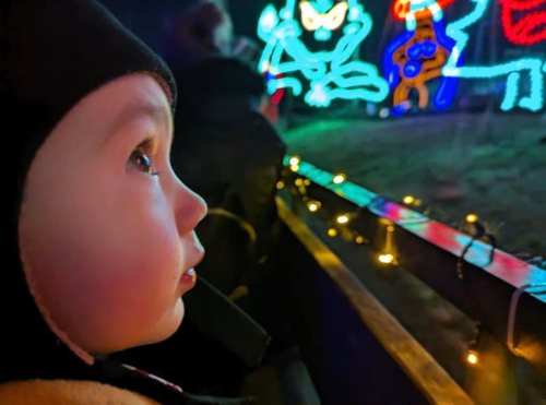 A child gazes in wonder at colorful holiday lights in the background, with a soft glow illuminating their face.