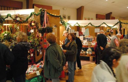 A bustling holiday market with vendors, decorations, and shoppers browsing various festive items.