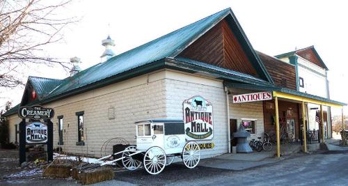A rustic building with a green roof, featuring signs for "Antique Mall" and "The Creamery," surrounded by vintage decor.