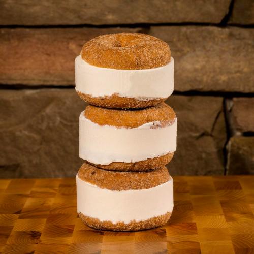 Three stacked donuts with a white cream filling, resting on a wooden surface against a stone background.