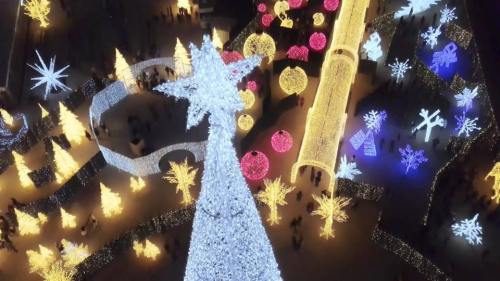 Aerial view of a festive display with illuminated trees, stars, and colorful ornaments in a winter wonderland setting.