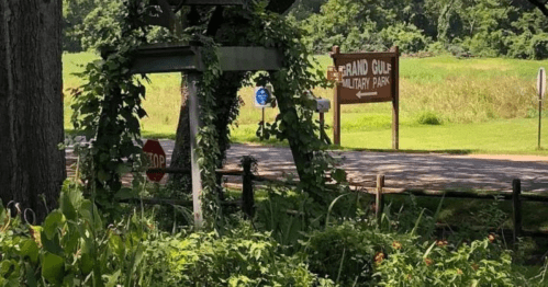A sign for Grand Gulf Military Park is visible through greenery, with a stop sign nearby and a grassy field in the background.