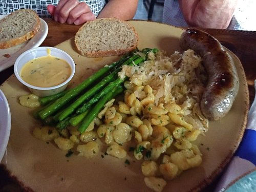 A plate of food featuring sausage, sauerkraut, asparagus, gnocchi, and a slice of bread with a dipping sauce on the side.