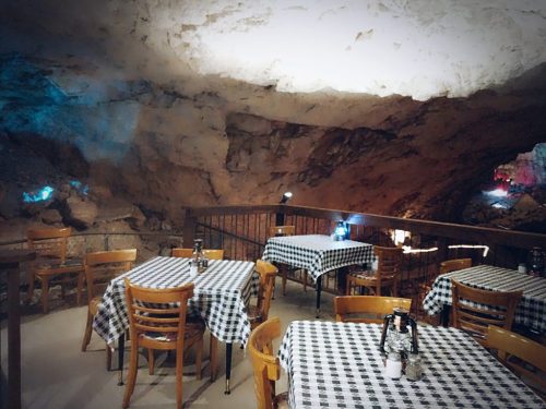A cozy cave restaurant with wooden tables and checkered tablecloths, illuminated by soft lights in the rocky surroundings.