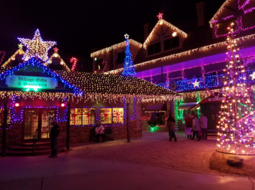 A festive scene with buildings adorned in colorful holiday lights and decorations, including a large illuminated tree.