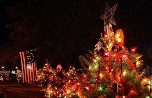 A brightly lit Christmas tree with a star on top, surrounded by colorful lights and a flag in the background.