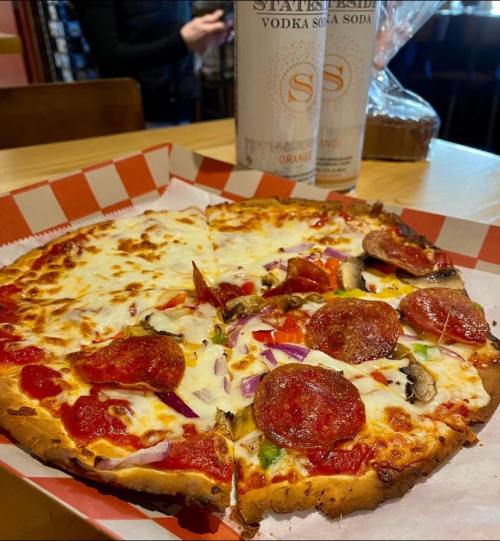 A freshly baked pepperoni pizza with cheese, vegetables, and a can of soda in the background on a wooden table.