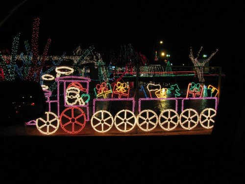 Colorful holiday lights form a train with festive decorations, set against a dark night sky.