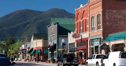 A charming small-town street lined with shops and restaurants, set against a backdrop of mountains.