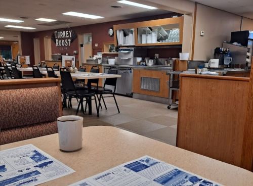 A cozy diner interior with empty tables, a coffee cup, and a visible kitchen area in the background.