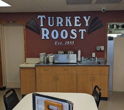 Interior of a diner with a "Turkey Roost" sign, wooden cabinets, and a serving area. Established in 1955.