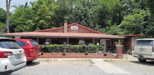 A rustic building with a red metal roof, surrounded by greenery and parked cars, labeled "The Old Glass House."