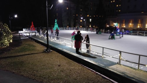People ice skating at night on a rink decorated with colorful lights and festive trees.