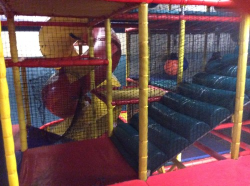 Colorful indoor play structure with slides and climbing areas, enclosed in netting for safety.