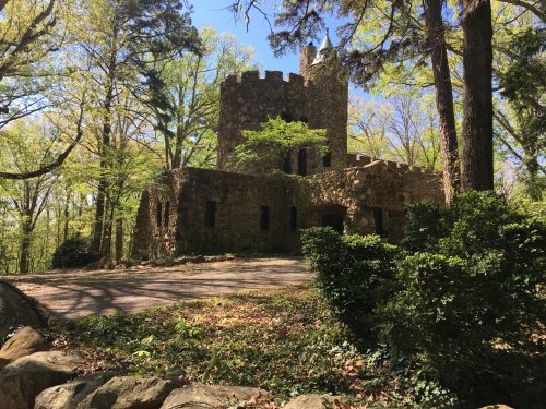 A stone castle surrounded by trees and greenery, set in a peaceful, wooded area on a sunny day.