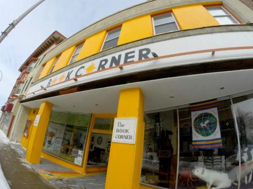 A colorful storefront with the sign "The Book Corner" and a display window, featuring books and a white object inside.