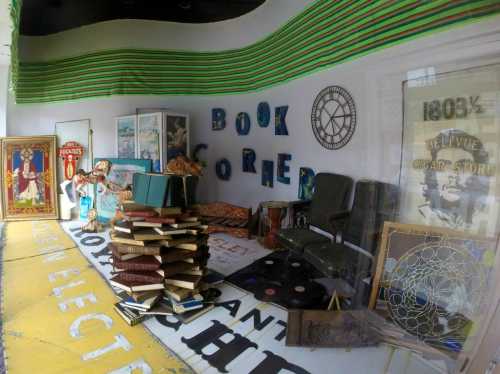 A cozy book corner with stacked books, vintage decor, and seating, set against a colorful wall and floor.