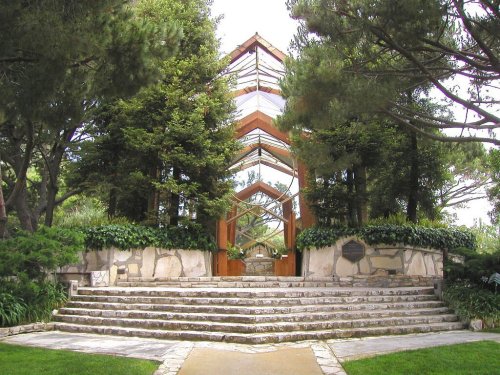 A modern architectural structure surrounded by trees and greenery, featuring stone steps leading up to it.