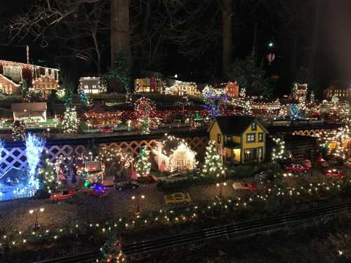 A festive miniature village illuminated with colorful lights, featuring houses, trees, and toy cars.