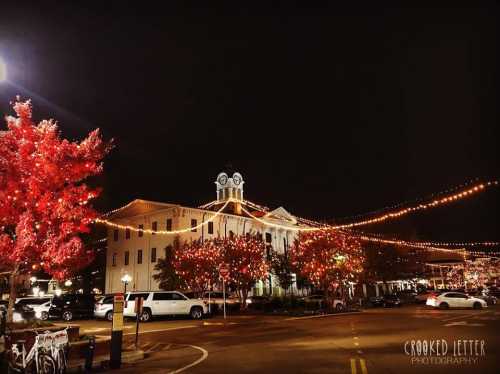 A charming night scene featuring a lit-up building and red trees, adorned with festive lights along a quiet street.