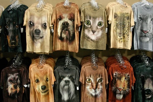 A display of t-shirts featuring large animal faces, including dogs, cats, and wild animals, hanging on racks.