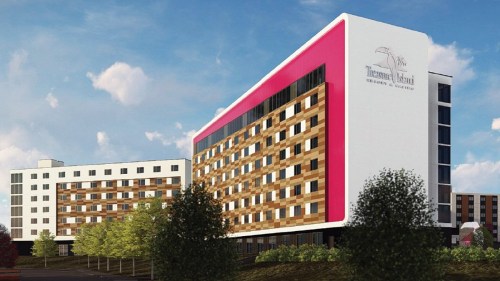 Modern hotel building with a pink and white facade, surrounded by trees and a clear blue sky.