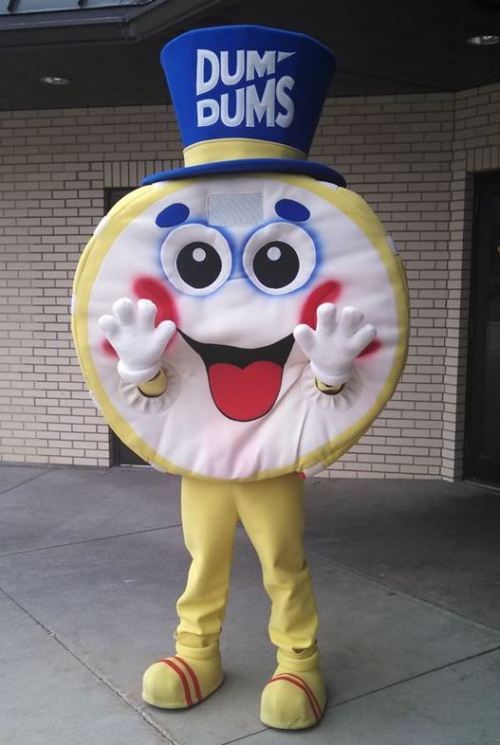 A cheerful mascot resembling a large lollipop, wearing a blue hat and yellow outfit, waving with a big smile.